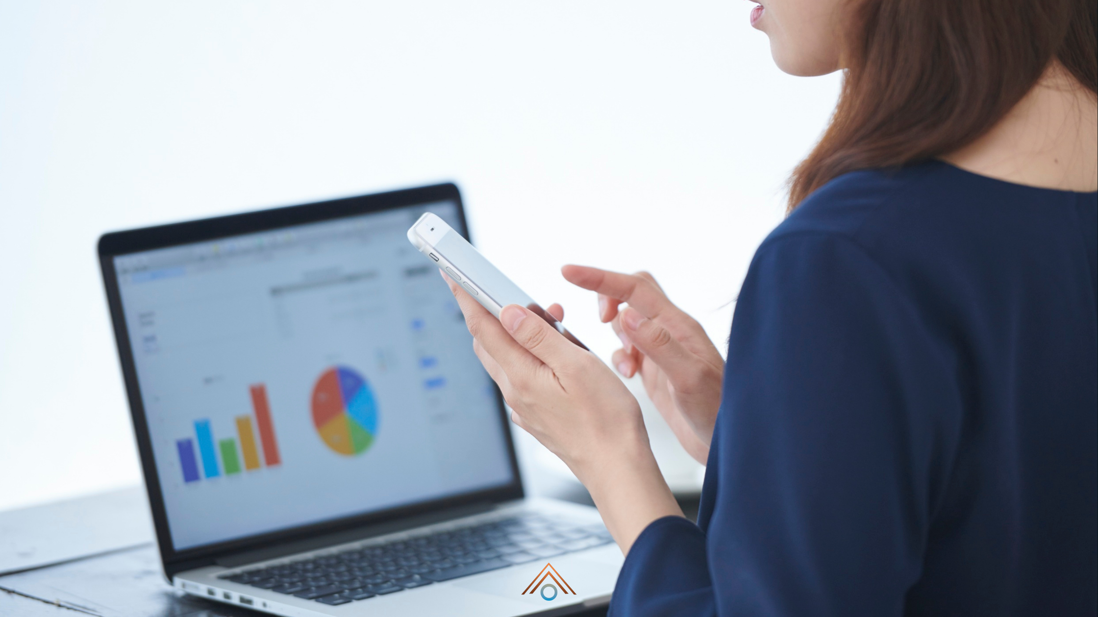 Uma varejista olhando algumas informações no celular e ao fundo um dashoard com gráficos no laptop